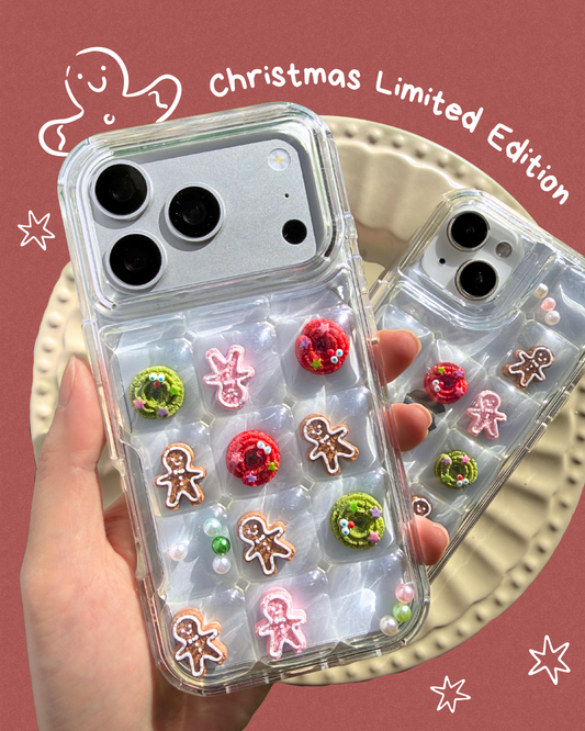 A hand holds two clear phone cases decorated with Christmas-themed embellishments, including gingerbread men, candy canes, and green wreaths, against a dusty rose background with decorative doodles and the text 'Christmas Limited Edition'.