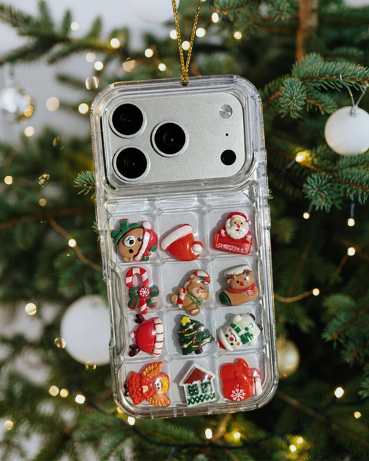 A hand holds two clear phone cases decorated with Christmas-themed embellishments, including gingerbread men, candy canes, and green wreaths, against a dusty rose background with decorative doodles and the text 'Christmas Limited Edition'.