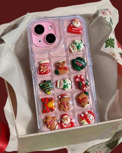 Two clear phone cases decorated with small red and green holiday embellishments and pink gingerbread figures, shown on a beige plate against a dusty rose background with gingerbread line drawings.